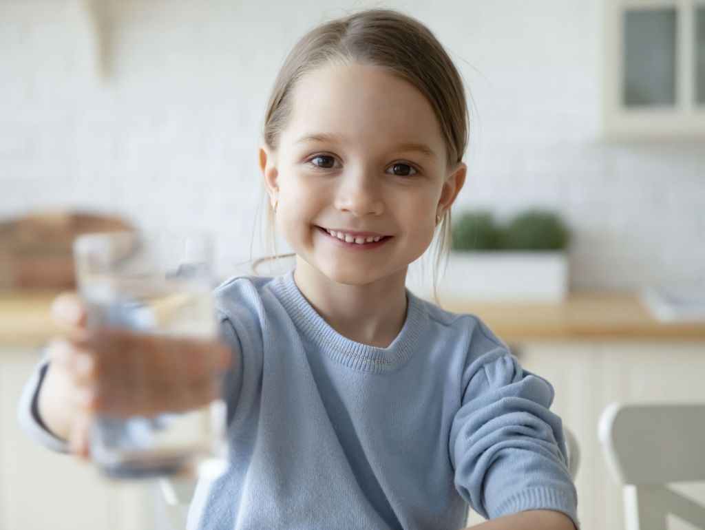Ein junges Mädchen hält lächelnd ein Glas Wasser in der Hand