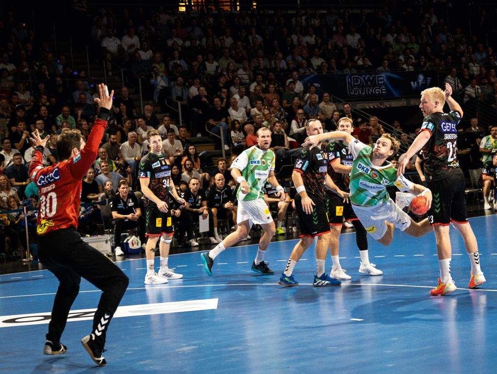Eine Gruppe von Männern, die auf einem Platz Handball spielen, dribbeln, schießen und gegeneinander antreten